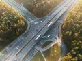 Widok z lotu ptaka na węzeł autostradowy otoczony jesiennym lasem, z ruchem samochodowym.