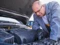 Mechanik w okularach naprawia silnik samochodu pod otwartą maską.