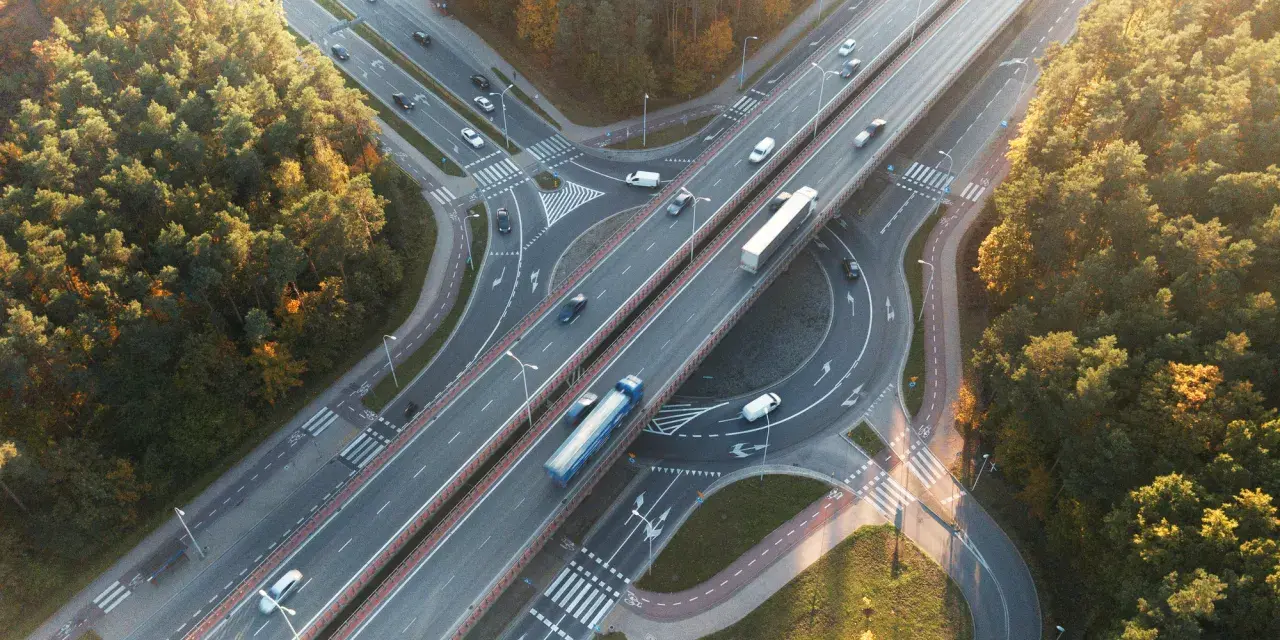 Widok z lotu ptaka na węzeł autostradowy otoczony jesiennym lasem, z ruchem samochodowym.