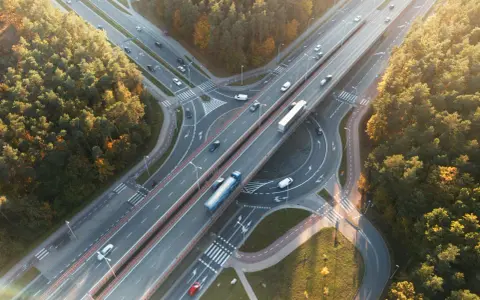 Widok z lotu ptaka na węzeł autostradowy otoczony jesiennym lasem, z ruchem samochodowym.