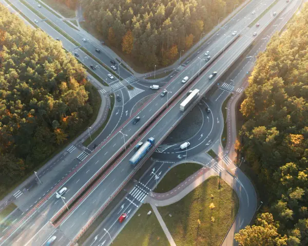Widok z lotu ptaka na węzeł autostradowy otoczony jesiennym lasem, z ruchem samochodowym.