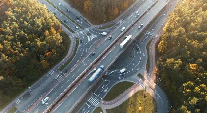 Widok z lotu ptaka na węzeł autostradowy otoczony jesiennym lasem, z ruchem samochodowym.